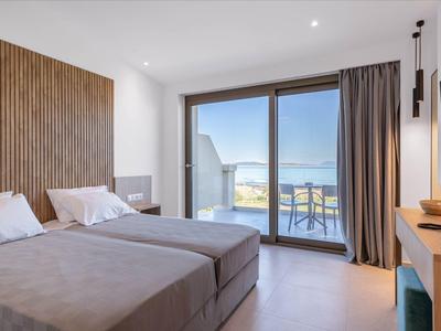 Moderne hotelkamer met twee bedden en balkon met zeezicht via glazen deuren.