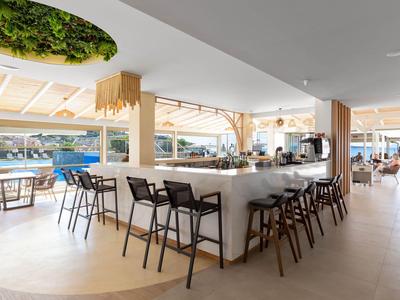 Área de bar de hotel moderna y luminosa con sillas, mesas y vista al mar.