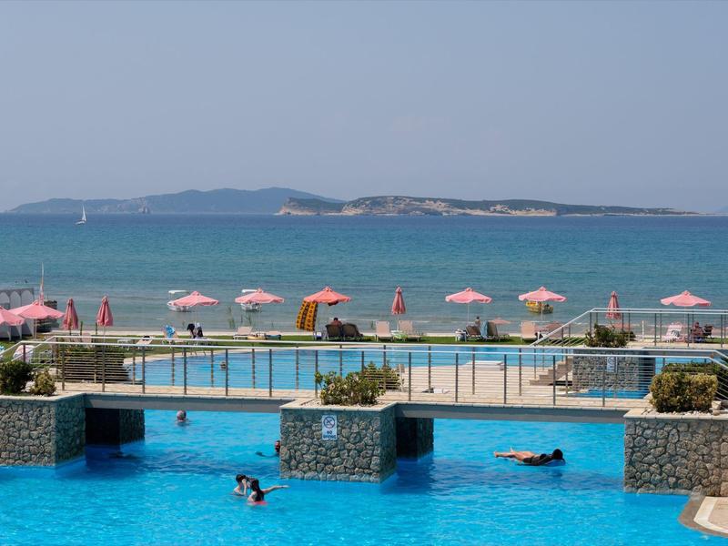 Zwembad met zwemmers, ligstoelen, parasols en uitzicht op zee en eilanden.