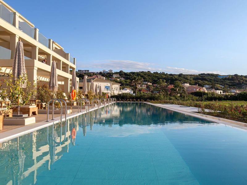 Buitenzwembad bij een resort met ligstoelen en groene heuvels in de verte.
