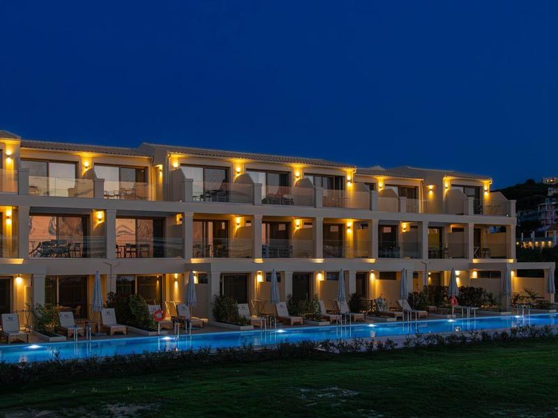 Hotelgebouw verlicht 's nachts met balkons en een zwembad ervoor, onder een donkerblauwe lucht.