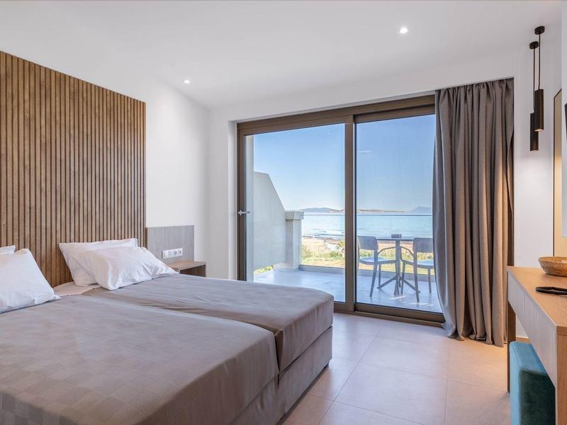 Moderne hotelkamer met twee bedden en balkon met zeezicht via glazen deuren.