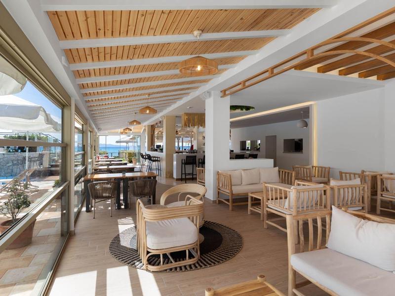 Lichte lounge binnen met houten meubels, grote ramen en uitzicht op zee.