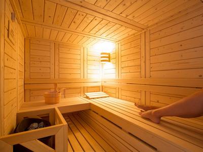 Holzsauna mit Sitzbänken, warmem Licht und einer Person, die entspannt liegt.