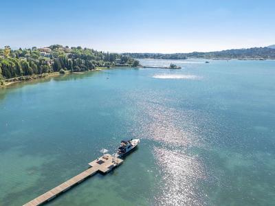 Blauer See mit Steg, grün bewaldeten Ufern und klarem Himmel im Hintergrund.