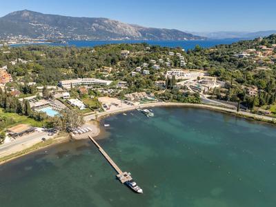 Bucht mit Steg, grünem Wasser, umgeben von Wäldern, Häusern und Bergen im Hintergrund.