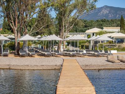 Molo vedoucí k plážové oblasti s deštníky a lehátky před hotelovou budovou.