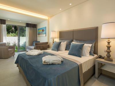 Helles Schlafzimmer mit großem Bett, blauen Kissen, Nachtischlampen und Terrasse mit Gartenblick.