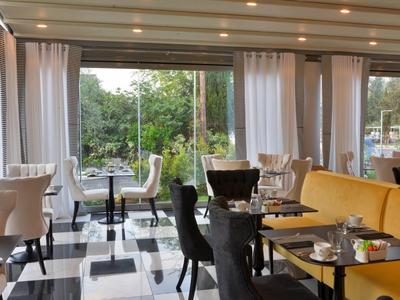 Helles Restaurant mit großen Fenstern, weißen Vorhängen, schwarz-weißen Fliesen und modernen Stühlen.