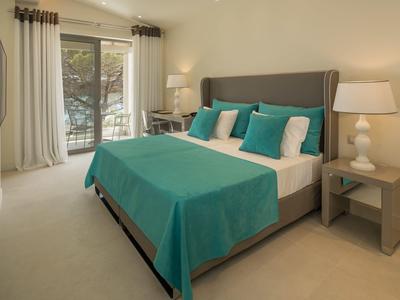 Modernes Schlafzimmer mit türkisfarbenem Bett, grauem Kopfteil, Nachttischen und großen Fenstern.