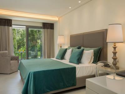 Modernes Schlafzimmer mit großem Bett, grünen Kissen, Stuhl und Fenster mit Blick auf Garten.