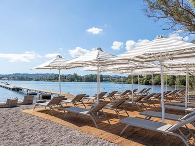 Lehátka pod slunečníky na pláži s výhledem na klidné jezero a hory