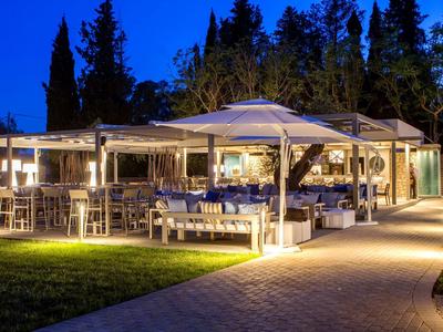 Beleuchtete Terrasse mit weißen Sonnenschirmen und Gartenmöbeln vor dunklem Wald in der Abenddämmerung.
