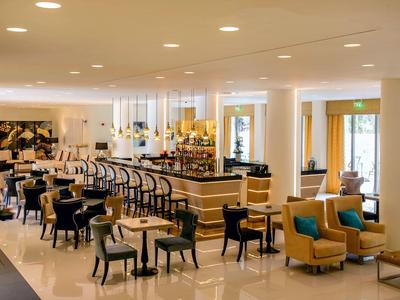 Elegantes Café mit Tischen, Stühlen und gemütlichen Sesseln in hellem, modernem Ambiente.