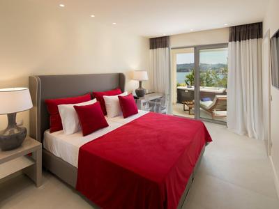 Modernes Schlafzimmer mit großem Bett, roter Bettwäsche, Nachttischen, Lampen und Balkon mit Aussicht.