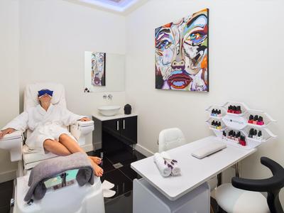 Eine Frau in Bademantel entspannt auf Sessel in einem modernen Nagelstudio mit buntem Wandbild.