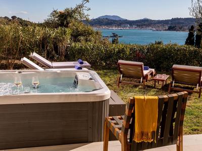 Whirlpool auf Terrasse mit Holzstuhl, Decke, Gartenmöbeln und See im Hintergrund.