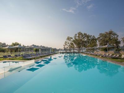 Velký venkovní bazén s lehátky a stromy na pozadí pod jasnou oblohou.