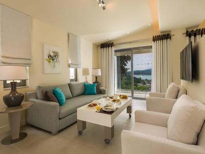 Helles Wohnzimmer mit graßem Fenster, gemütlicher Couch, weißen Sesseln und moderner Dekoration.