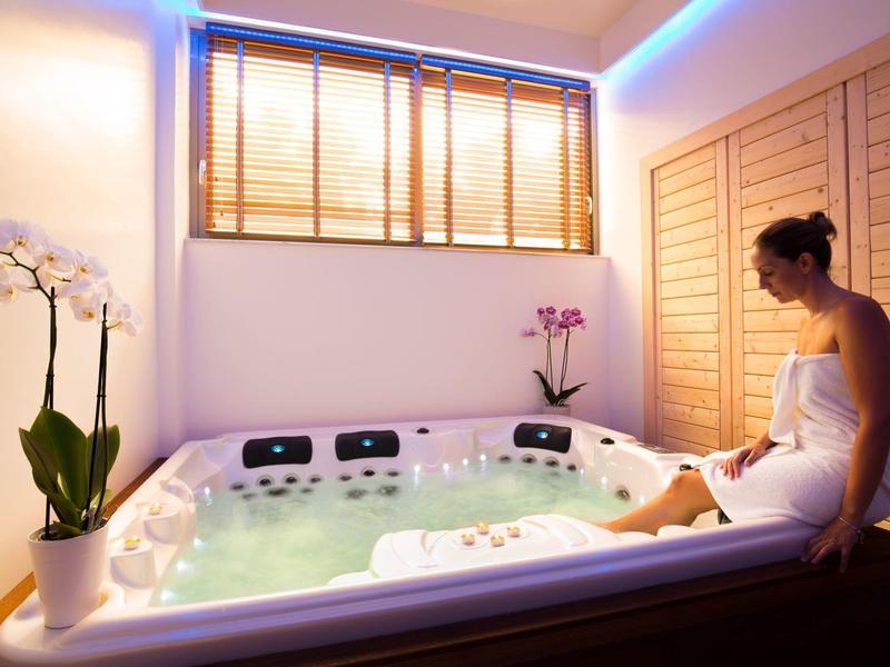 Moderner Whirlpool mit sprudelndem Wasser in hellem Raum, Pflanzen und weichem blauem Licht.