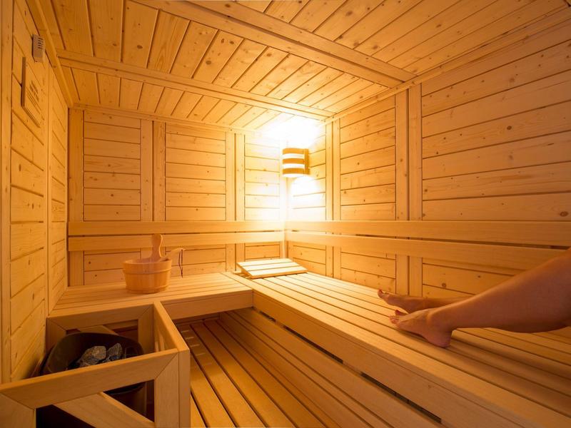 Holzsauna mit Sitzbänken, warmem Licht und einer Person, die entspannt liegt.