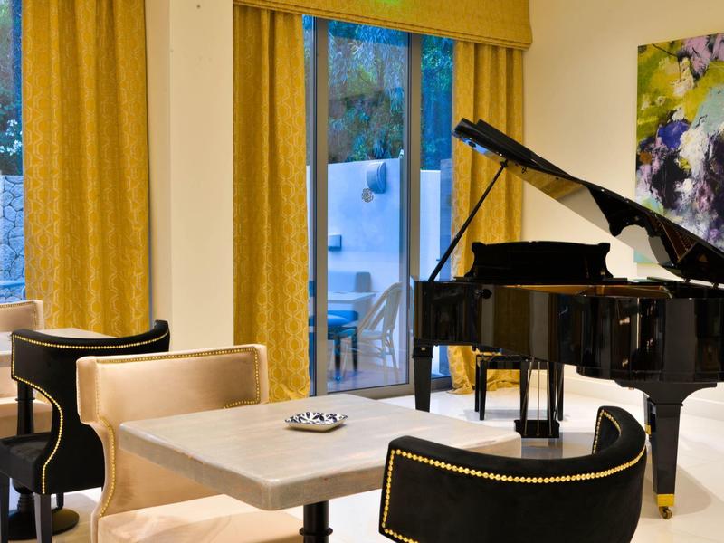 Eleganter Raum mit schwarzem Flügelklavier, beigen Sesseln, Tisch und gelben Vorhängen.