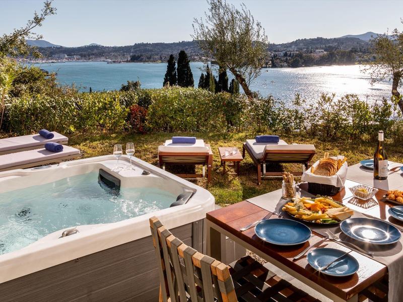 Terrasse mit Whirlpool, gedecktem Holztisch und Meerblick bei Sonnenschein.