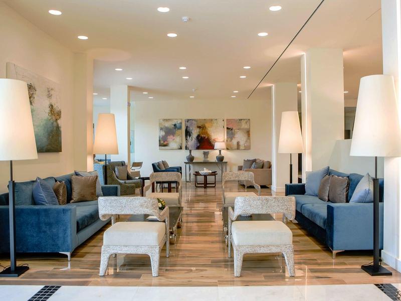 Moderner, heller Wohnraum mit blauen Sofas, weißen Hockern und stilvollen Stehlampen.