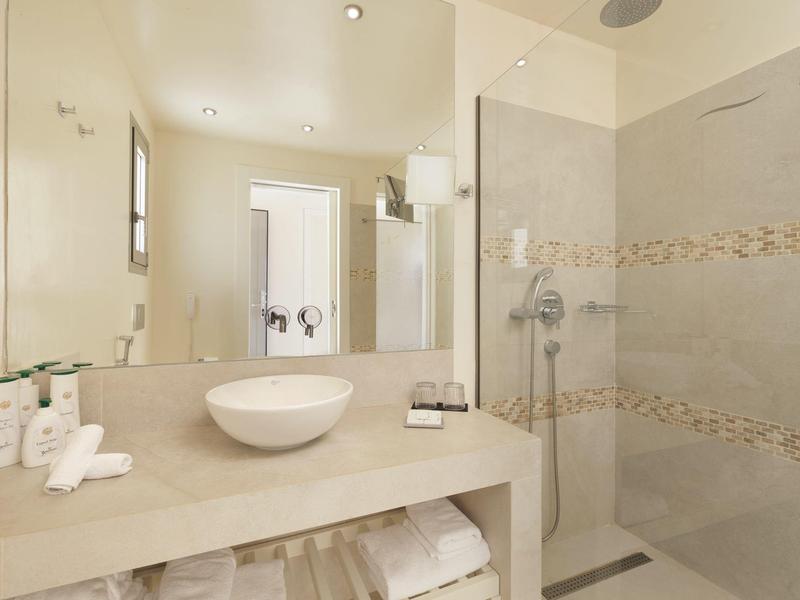 Helles Badezimmer mit großem Spiegel, weißem Waschbecken, Handtüchern und begehbarer Dusche.