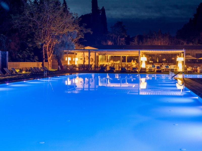 Beleuchteter Außenpool bei Nacht mit Gebäude und Bäumen im Hintergrund.