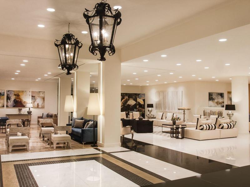 Großes, helles Wohnzimmer mit modernen Lampen, Sofas und Glasreflexion an der Wand.