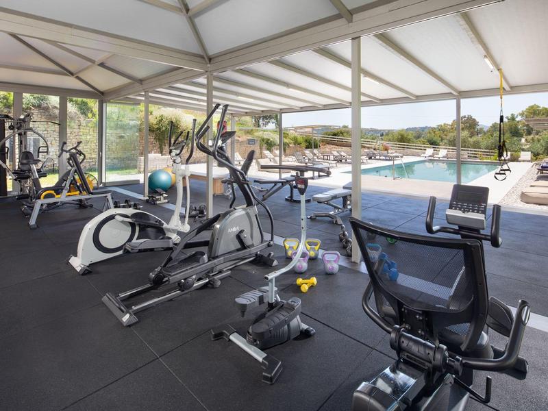 Fitnessraum mit modernen Geräten und Blick auf einen Außenpool, helle und offene Struktur.