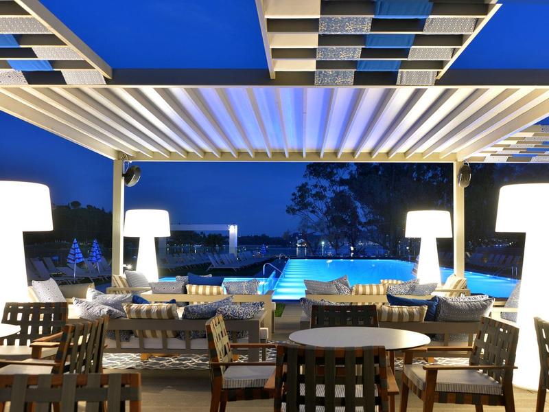 Moderner Außenbereich mit beleuchteten Tischen, Stühlen und Swimmingpool bei Abenddämmerung.