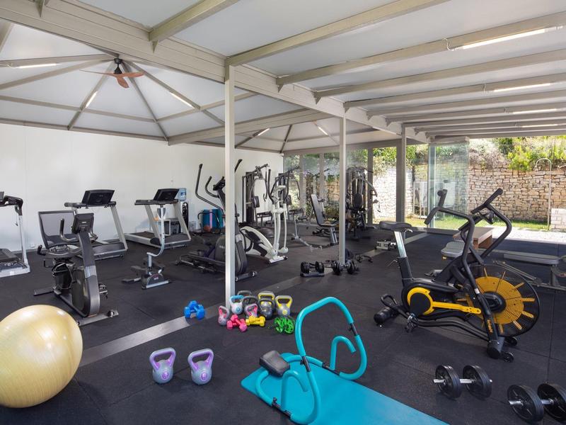 Fitnessraum mit verschiedenen Trainingsgeräten, Yoga-Matte und Hanteln, helle und offene Atmosphäre.