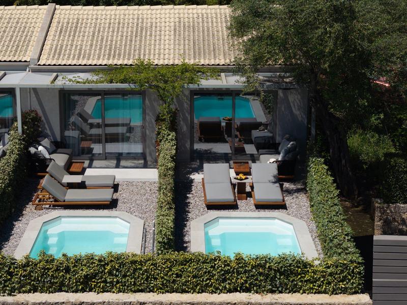 Zwei gleich große Pools mit Liegestühlen und Sonnenschirmen, umgeben von grünen Hecken.