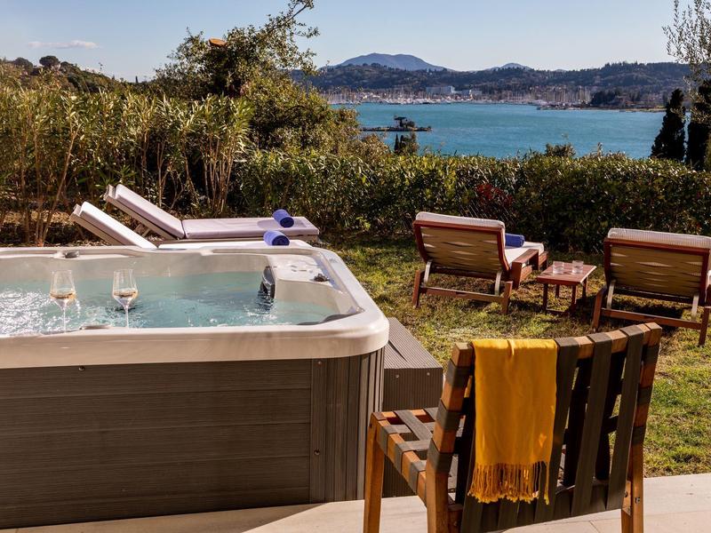 Whirlpool auf Terrasse mit Holzstuhl, Decke, Gartenmöbeln und See im Hintergrund.