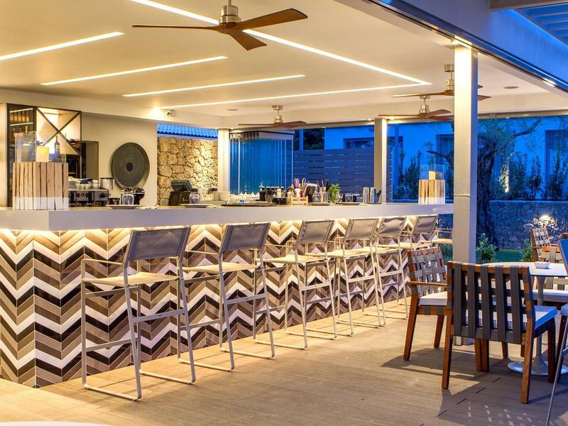 Moderner Außenbarbereich mit geometrischer Theke, Barhockern und gedecktem Tisch bei Abendlicht.