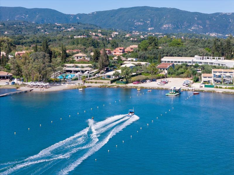 Klares blaues Meer mit zwei Jetskis, die Wellen vor einer grünen Küstenlandschaft ziehen.