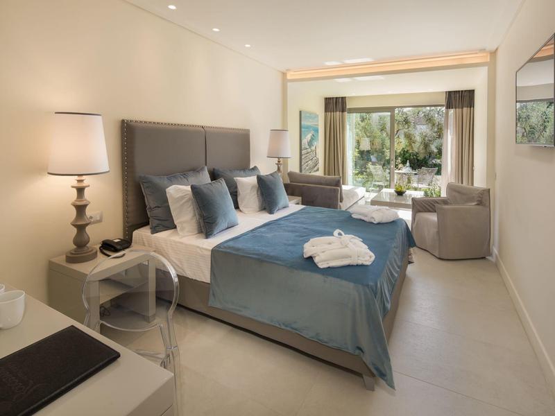 Modernes Schlafzimmer mit grauem Bett, blauen Kissen, Nachttischlampe und Blick auf Garten.