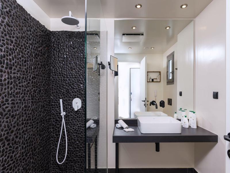 Modernes Badezimmer mit schwarzer Steinwand-Dusche, weißem Waschbecken und großen Spiegeln.