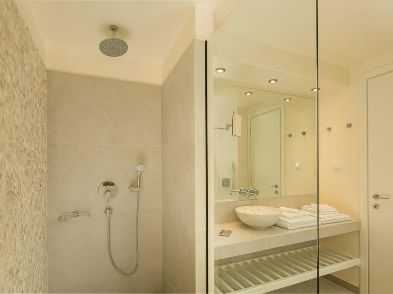 Modernes Badezimmer mit Glasdusche, weißem Waschbecken, Wandspiegel und heller Beleuchtung.