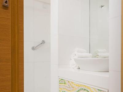 Weißes Badezimmer mit modernem Waschbecken, großer Spiegel und bunter Musterverkleidung.
