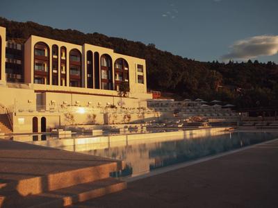 Großes Hotelgebäude mit Bogenfenstern neben einem leeren Pool in warmem Abendlicht.