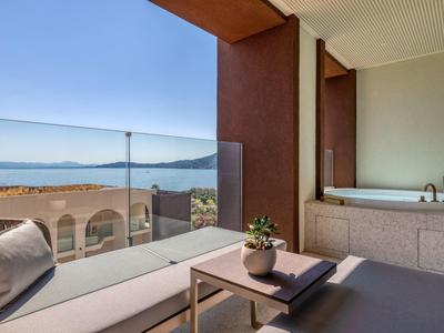 Moderner Balkon mit Glasgeländer, gemütlicher Sitzbank, kleinem Tisch und Whirlpool mit Meerblick.