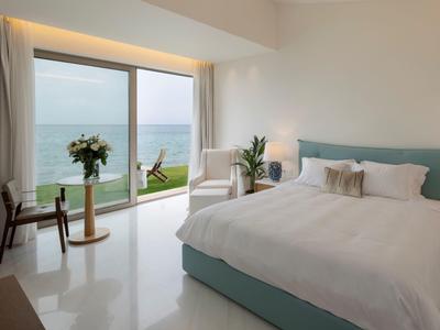 Helles Schlafzimmer mit großem Fenster, Doppelbett, Stuhl, Tisch und Meerblick in ruhiger Umgebung.