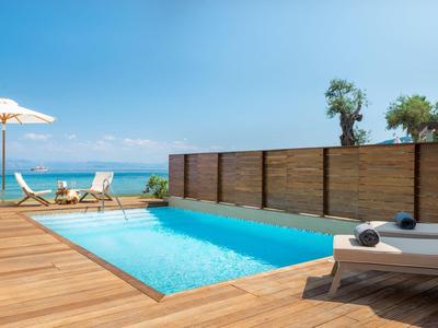 Moderner Pool mit Holzterrasse, Liegestühlen, Sonnenschirm und Blick aufs blaue Meer.