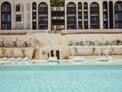 Großer Außenpool vor mehrstöckigem Hotel mit Balkonen und Liegestühlen am Rand.
