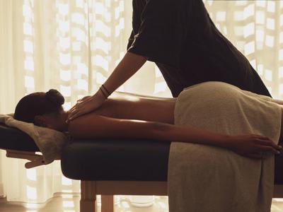 Eine Frau erhält eine Nackenmassage auf einer Massageliege vor einem hellen Vorhang.
