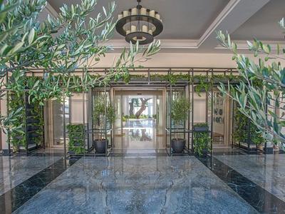 Modernes Hotelfoyer mit Glas-Eingangstüren, glänzendem Marmorfußboden und grünen Pflanzen.