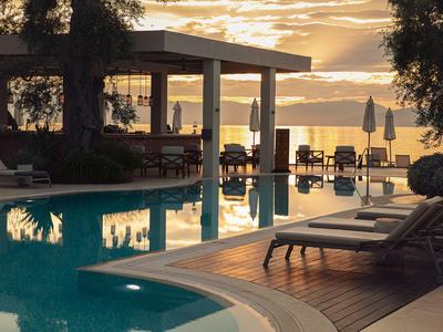 Hotelpool am Abend mit Liegestühlen und stimmungsvollem Sonnenuntergang über dem Wasser.